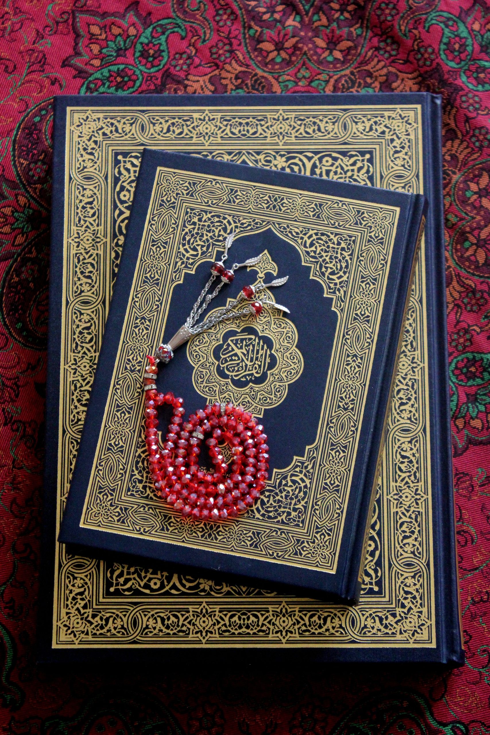 Ornate Quran placed on tapestry with red prayer beads, reflecting spirituality.