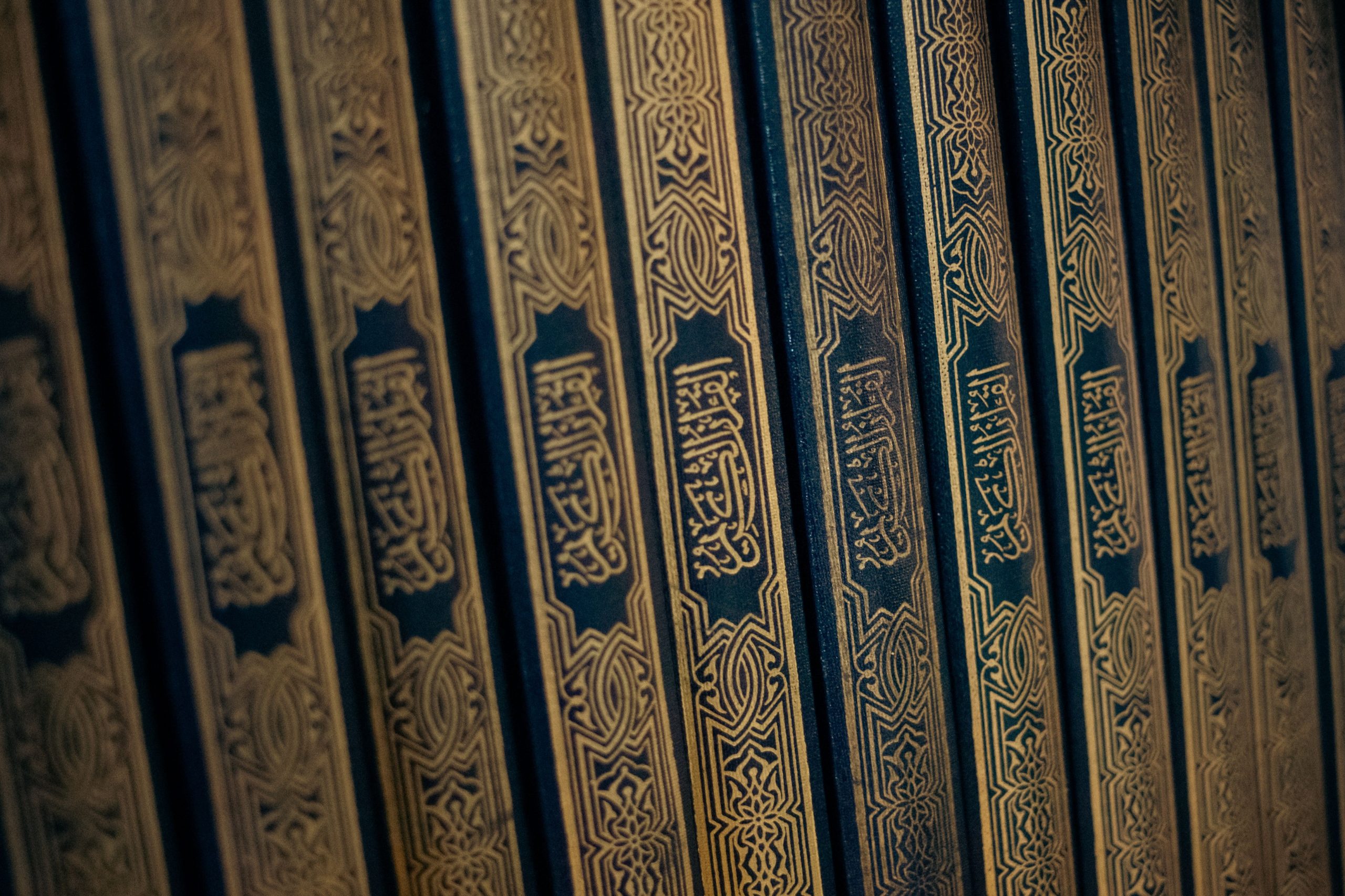 Close-up of Quranic book spines with ornate Arabic calligraphy, showcasing Islamic art and culture.