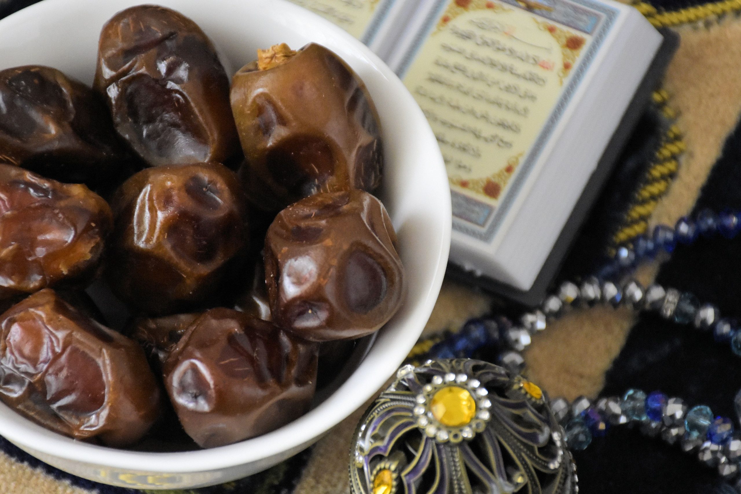Bowl of dates next to Quran and prayer beads, symbolizing Ramadan traditions.